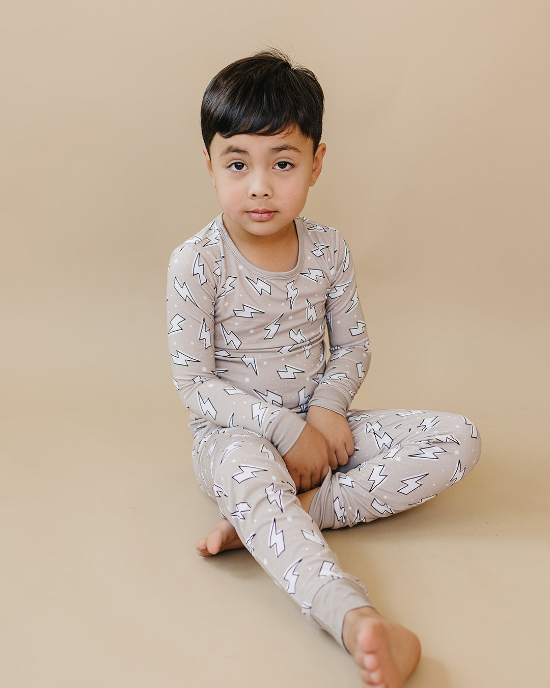 Child sitting cross-legged in the Latte Bolts bamboo two-piece set against a warm beige studio background.