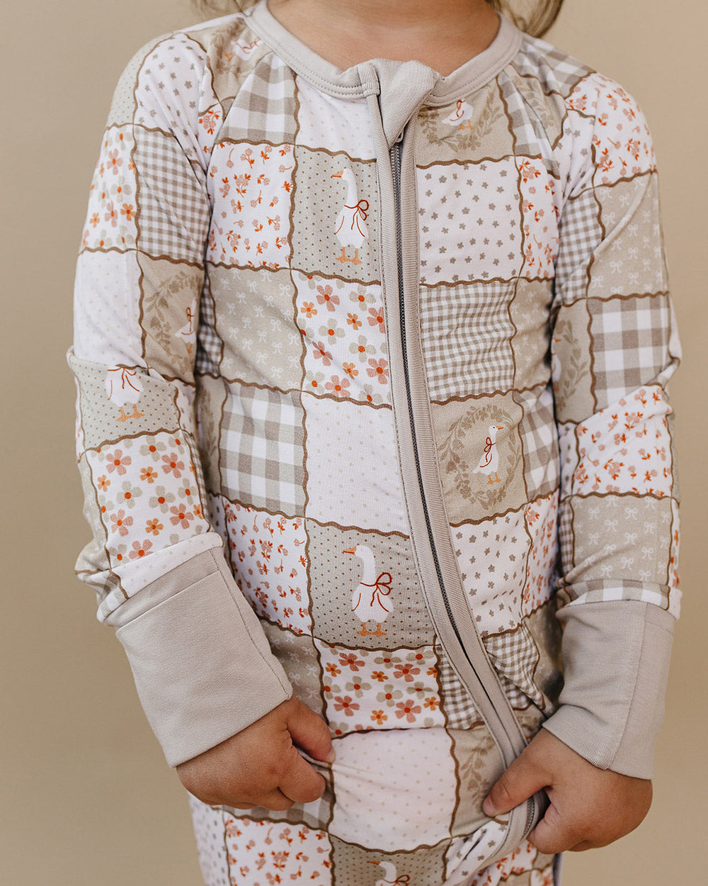 Close-up front view of the Cottage Goose bamboo zip romper, showing the two-way zipper and neutral patchwork print.