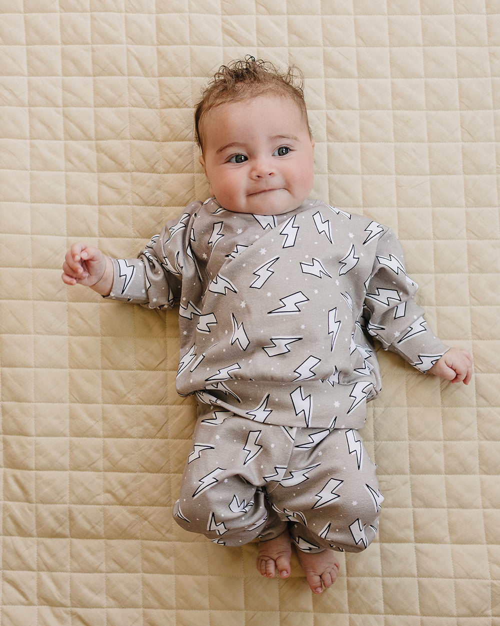 Baby boy lying on a beige quilt wearing the Latte Bolts cotton jogger set in a full-body view.