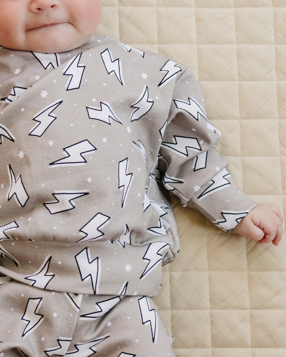 Close-up of a baby wearing the Latte Bolts jogger set, showing the crewneck top, elastic waist, and matching print.