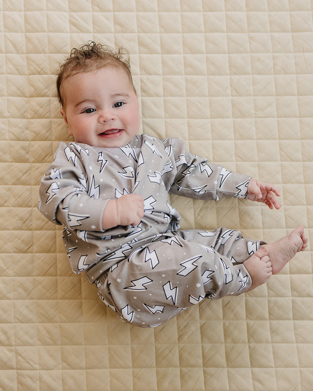 Close-up of a baby posing on a quilt in the Latte Bolts jogger set with the lightning bolt print clearly visible.