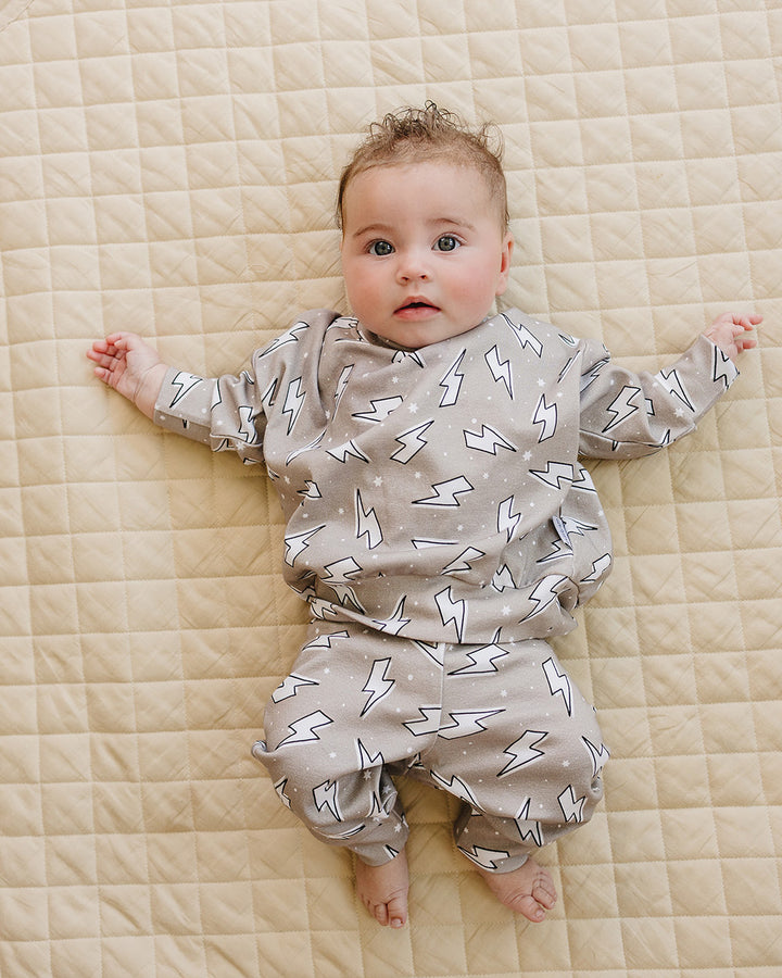 Baby boy lying with arms stretched out on a quilt while wearing the Latte Bolts cotton jogger set.