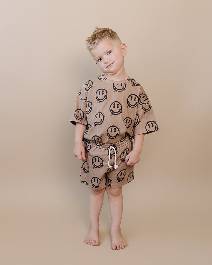 toddler boy wearing Lucky Panda Kids Smiley Brown Shorts Set — warm brown all-over smiley face print cotton two-piece outfit