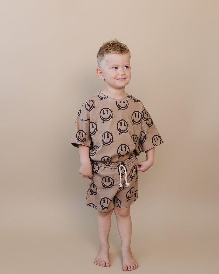 Toddler boy wearing Lucky Panda Kids Smiley Brown Shorts Set — warm brown all-over smiley face print cotton two-piece outfit