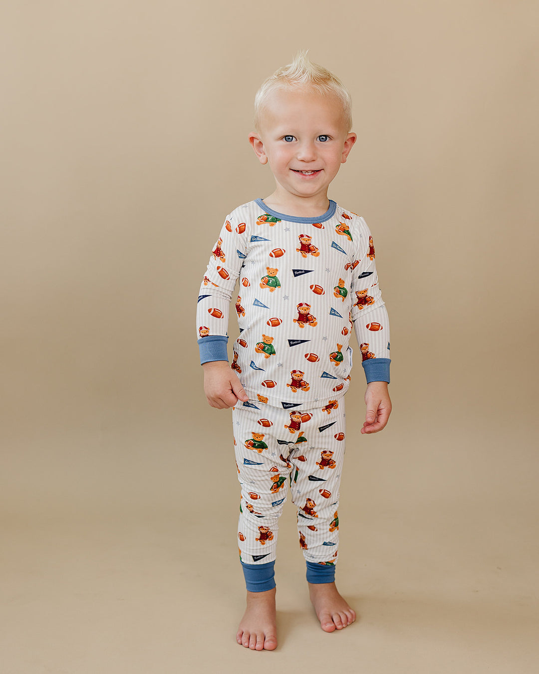 Full-length view of a toddler modeling the football and teddy bear-print bamboo outfit.