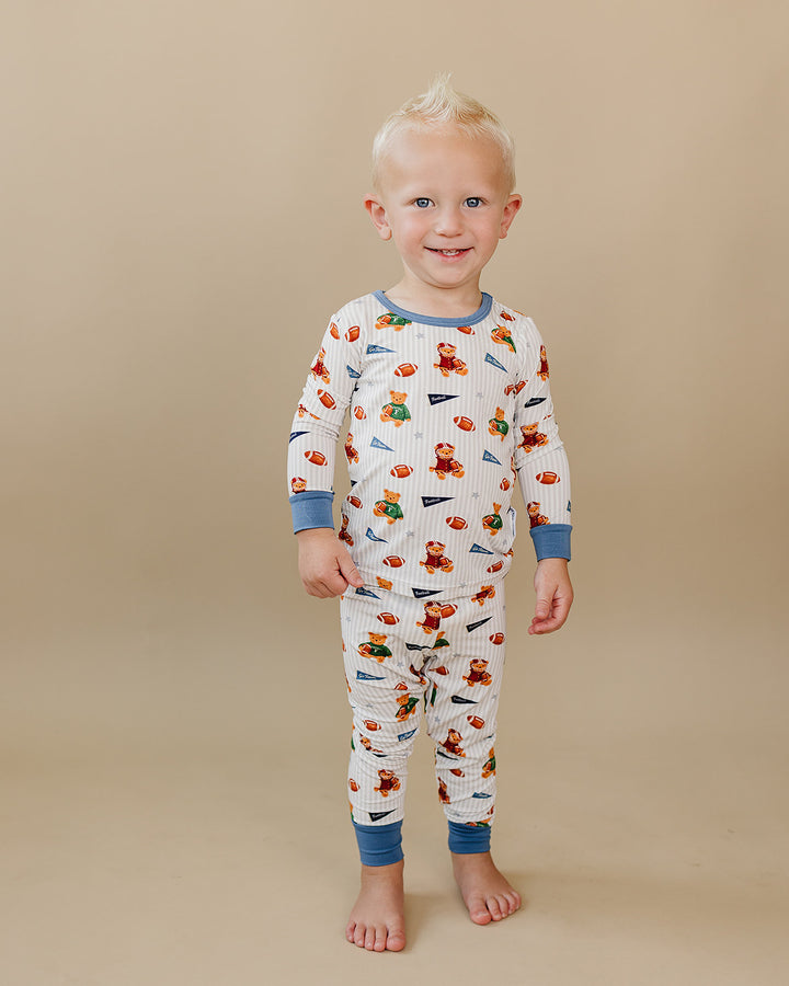 Full-length view of a toddler modeling the football and teddy bear-print bamboo outfit.