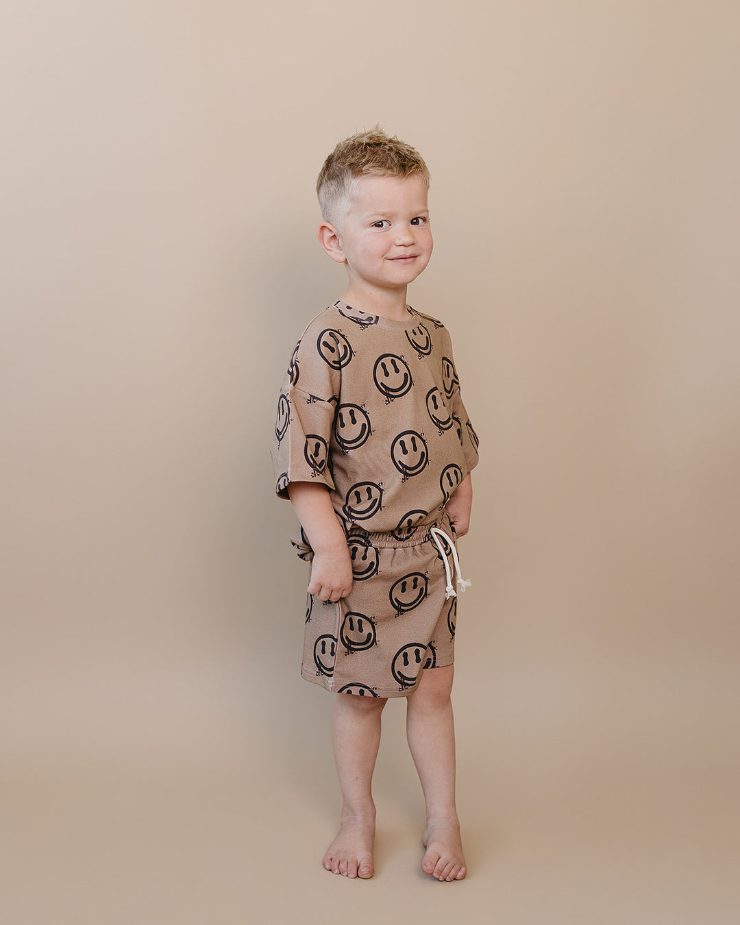 Toddler boy wearing Lucky Panda Kids Smiley Brown Shorts Set — warm brown all-over smiley face print cotton two-piece outfit