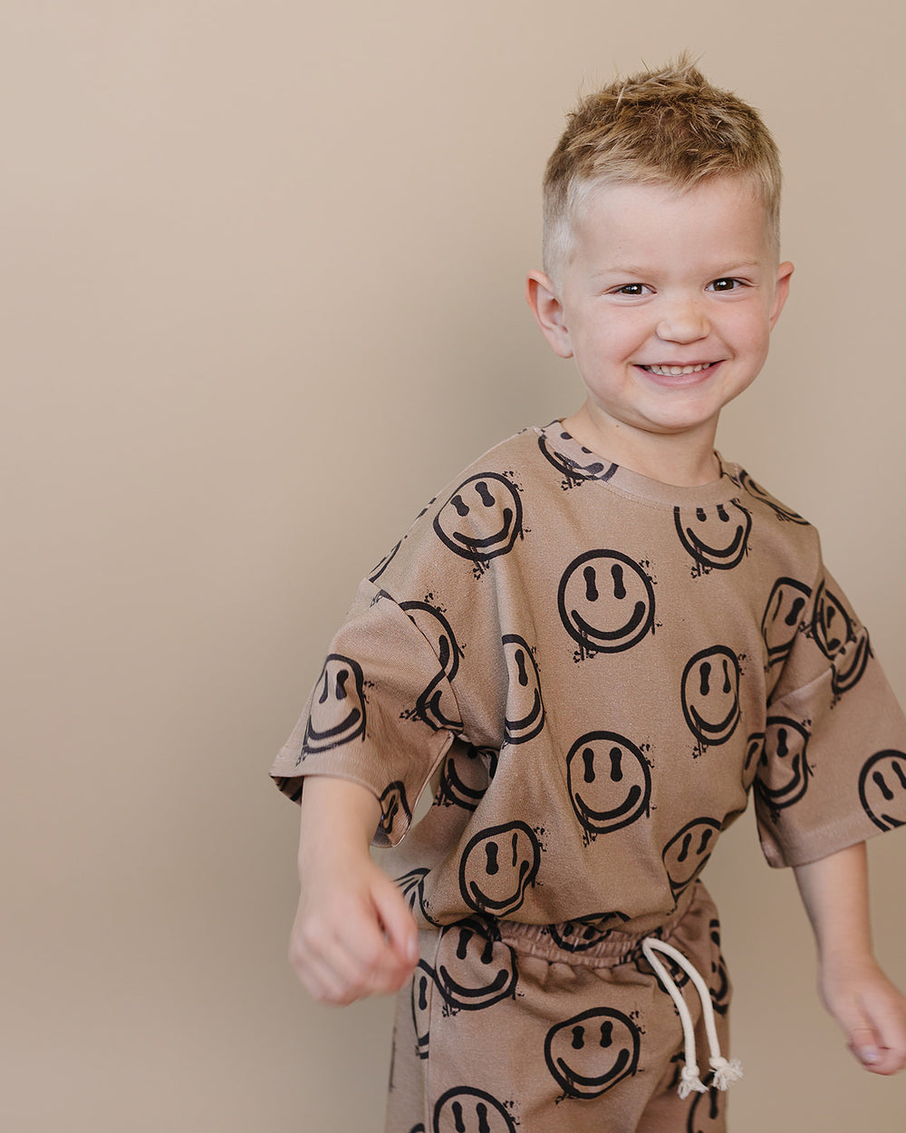 Toddler boy wearing Lucky Panda Kids Smiley Brown Shorts Set — warm brown all-over smiley face print cotton two-piece outfit
