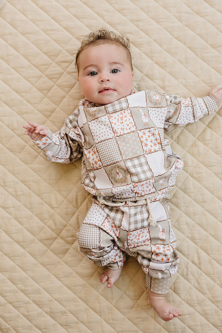 Full-body view of a baby girl lying on a quilt in the Cottage Goose cotton jogger set.