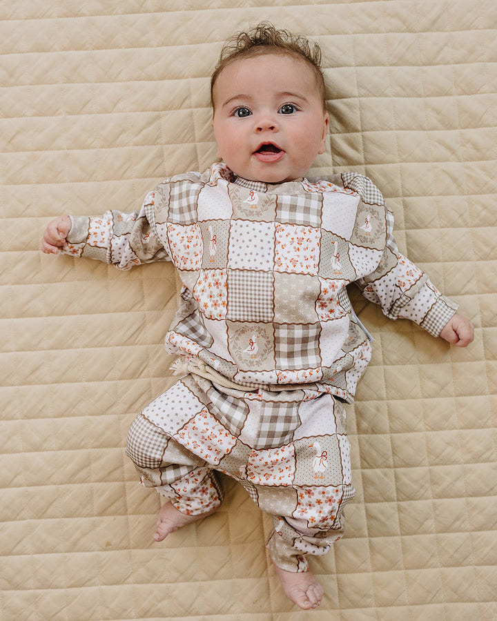 Baby girl sitting on a beige quilt in the Cottage Goose jogger set, showing the front fit and patchwork print.