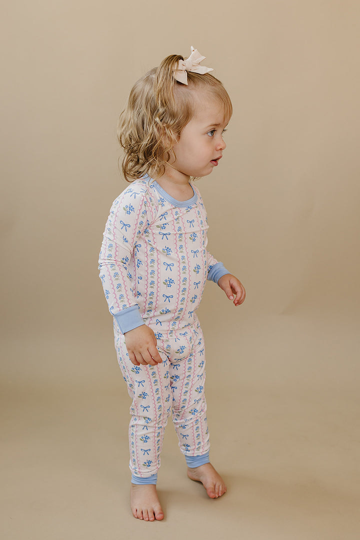 Toddler looking down while wearing the Whimsy Bloom floral bamboo two-piece set with light blue cuffs.