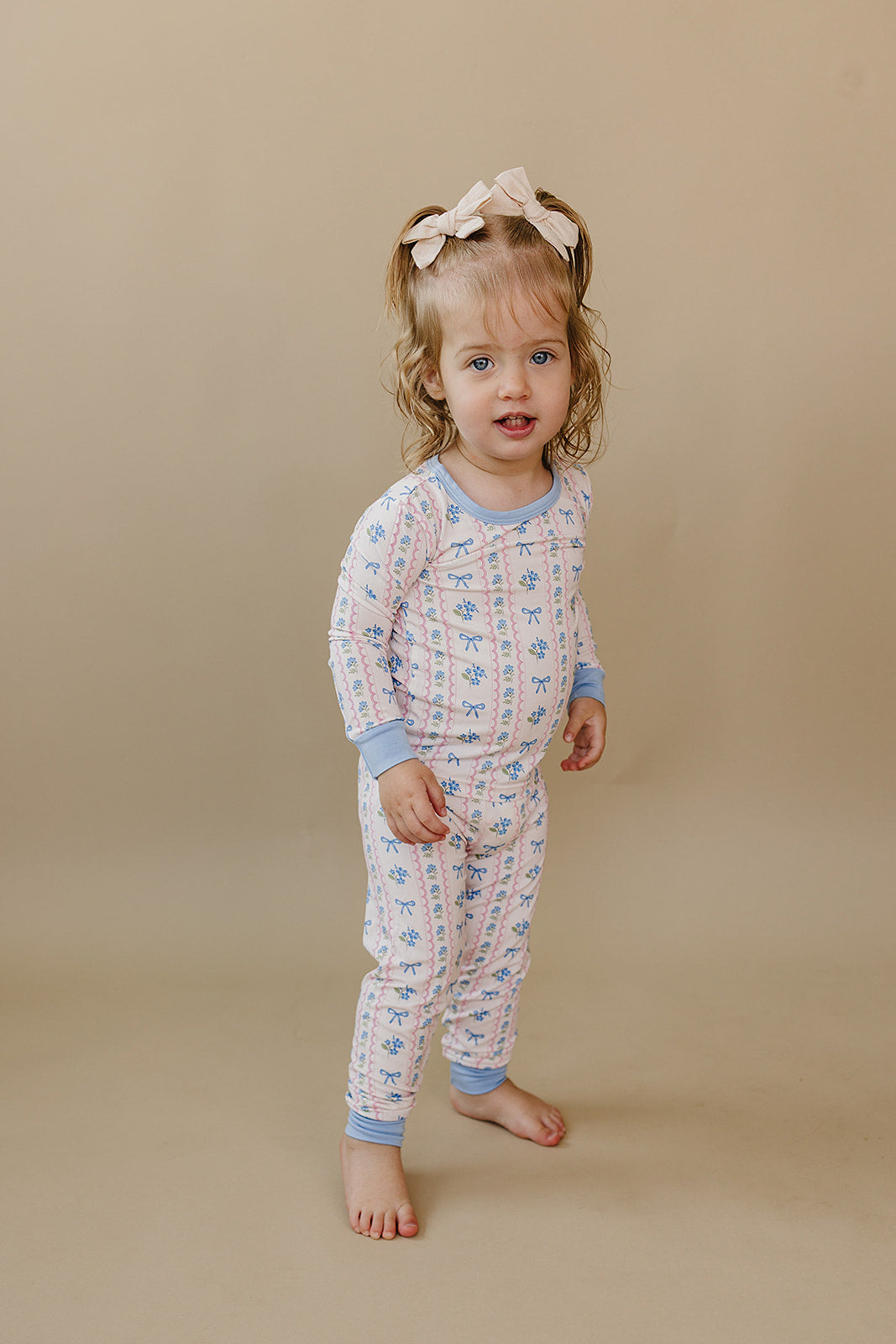 Toddler facing the camera in the Whimsy Bloom bamboo pajama set with pastel flowers and blue bows.