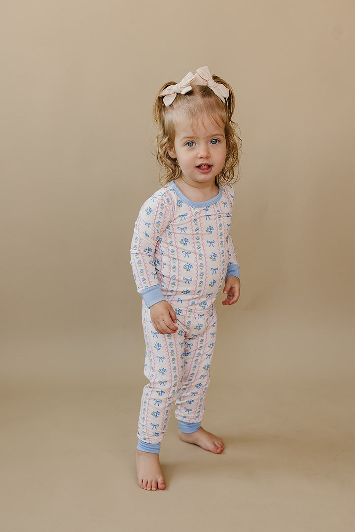 Toddler facing the camera in the Whimsy Bloom bamboo pajama set with pastel flowers and blue bows.