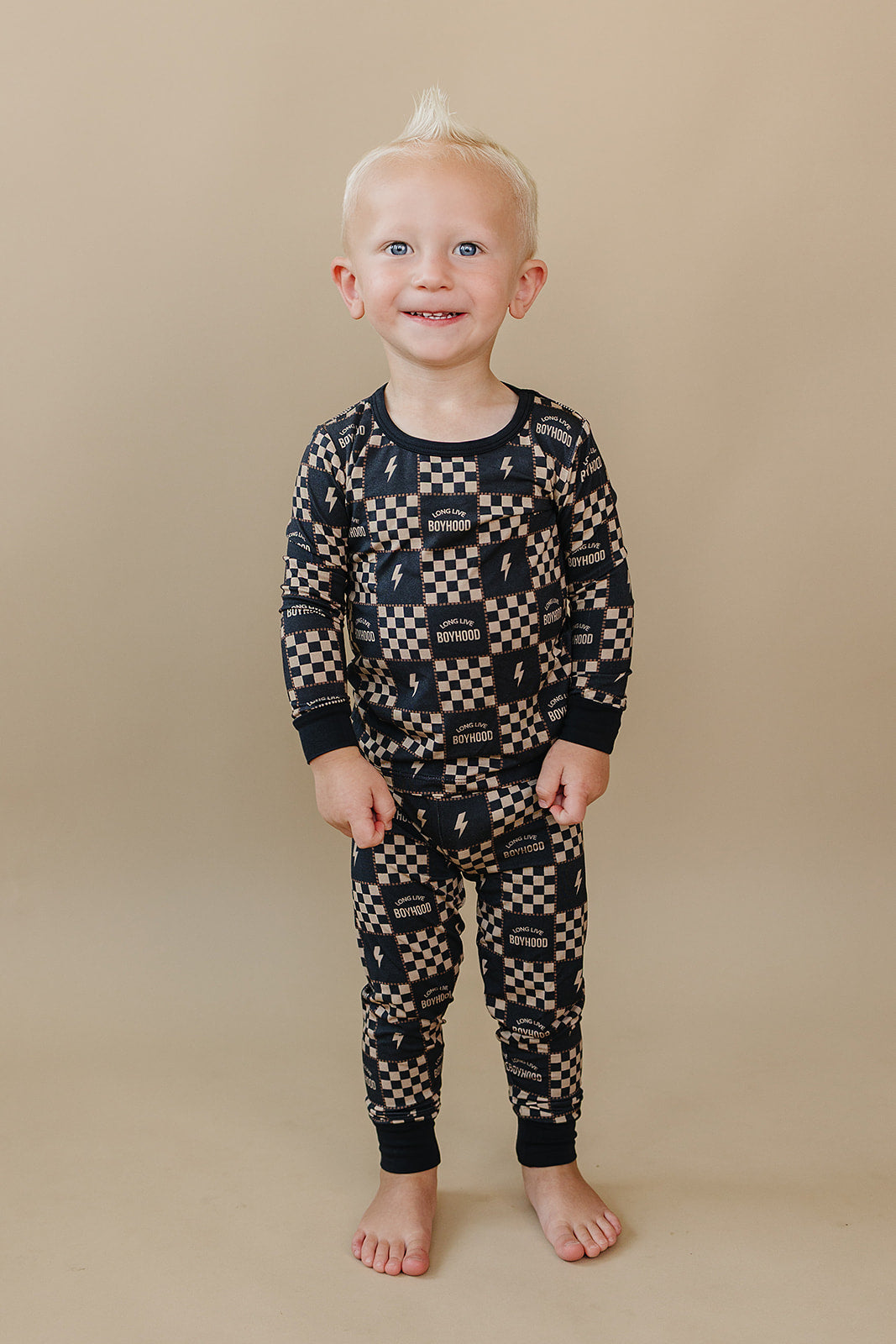 Smiling toddler standing in the Long Live Boyhood checkered bamboo two-piece set.