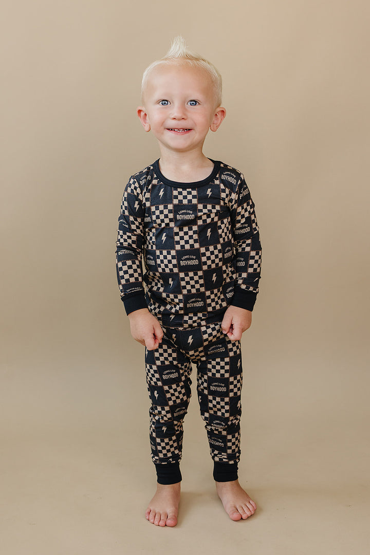 Smiling toddler standing in the Long Live Boyhood checkered bamboo two-piece set.
