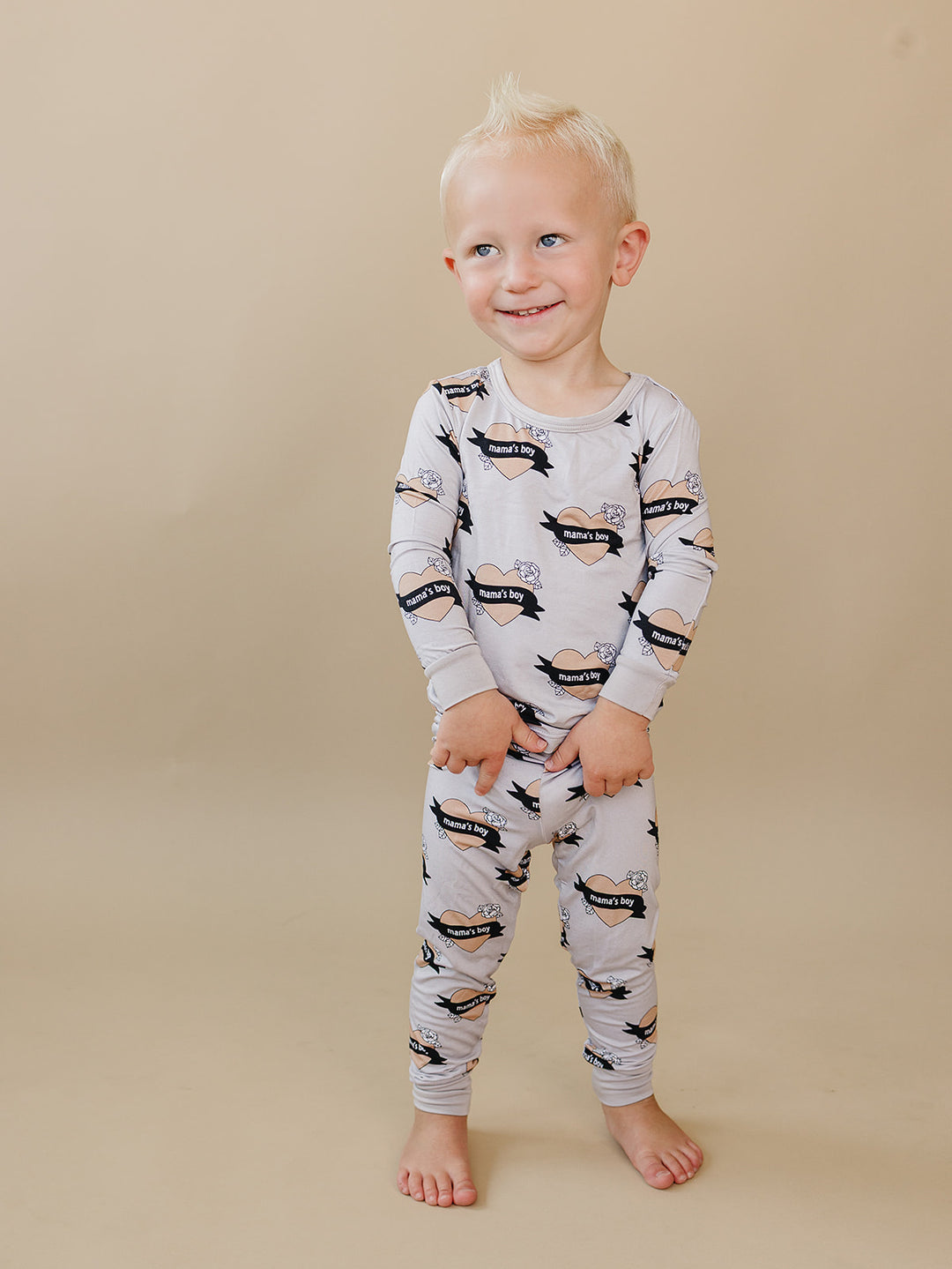Smiling toddler wearing the Mama’s Boy heart-print bamboo two-piece set.