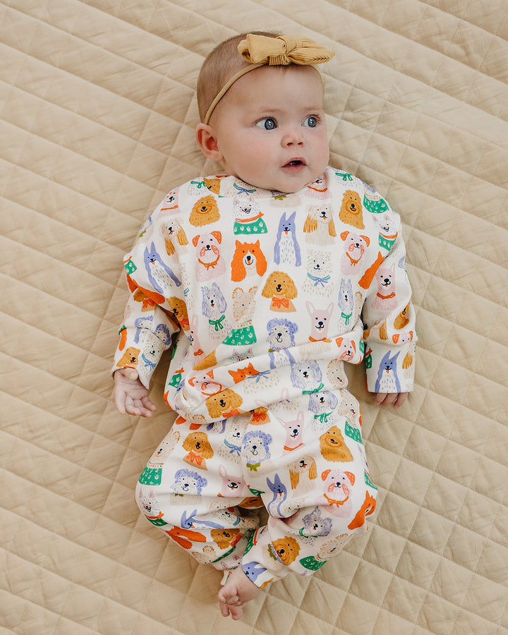 Baby looking to the side in the Puppy Club dog-print cotton outfit and mustard bow headband.