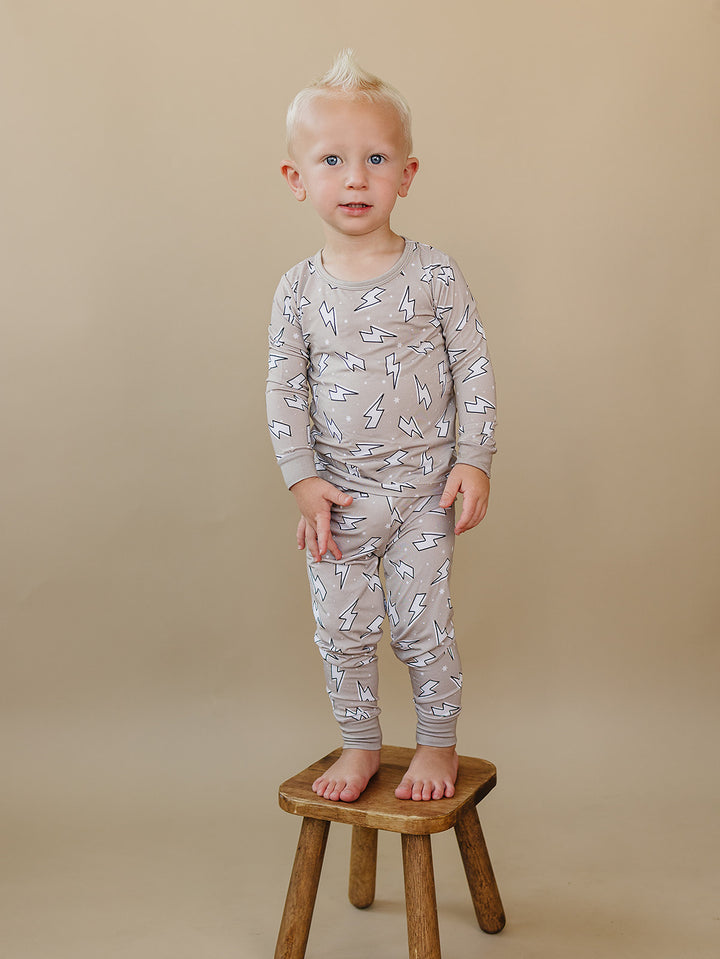 Smiling toddler standing on a small wooden stool while wearing the Latte Bolts bamboo two-piece set.
