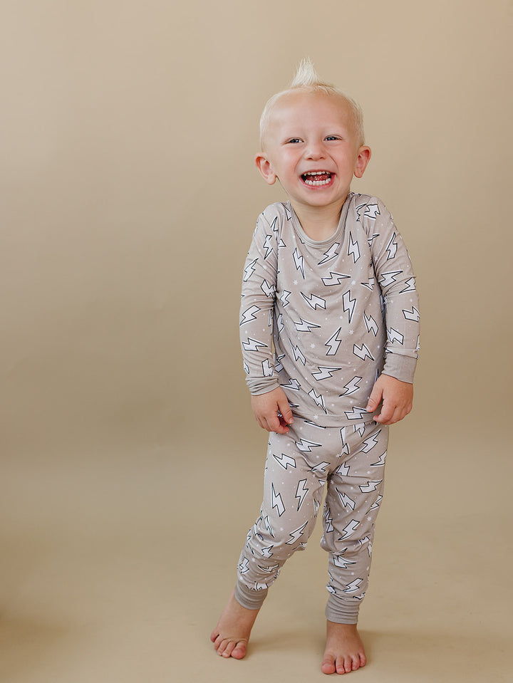 Smiling toddler modeling the Latte Bolts bamboo two-piece set against a neutral beige background.