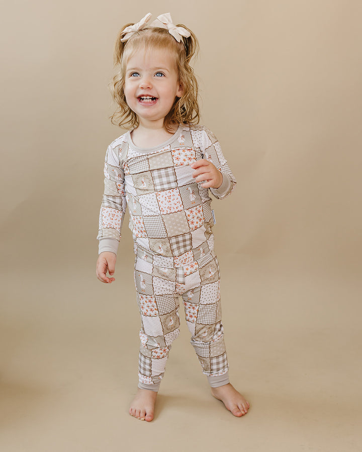 Smiling toddler standing barefoot in the Cottage Goose bamboo two-piece set against a warm beige background.