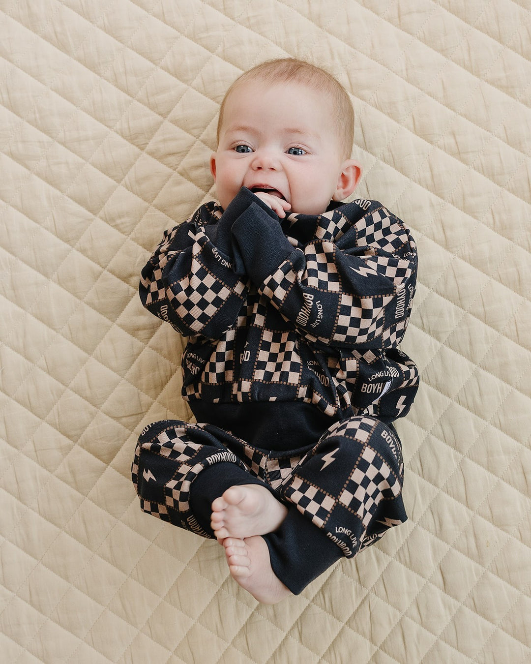 Baby with hands near their mouth wearing the Long Live Boyhood cotton top and matching jogger pants.