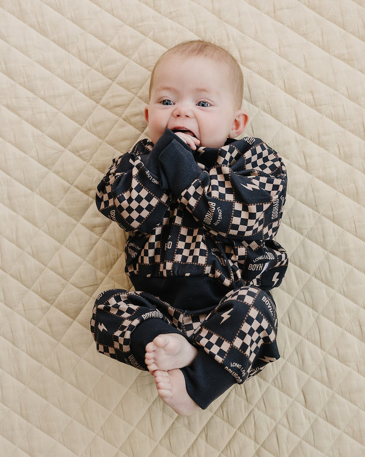 Baby with hands near their mouth wearing the Long Live Boyhood cotton top and matching jogger pants.