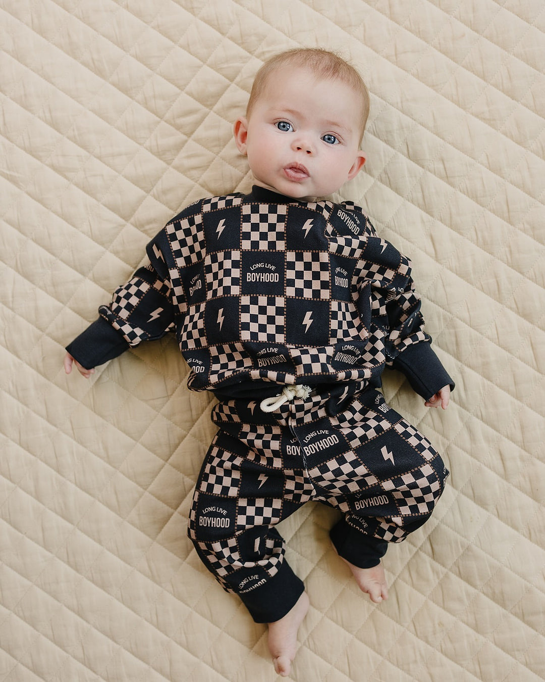 Baby lying with legs bent in the Long Live Boyhood checkered cotton jogger set.