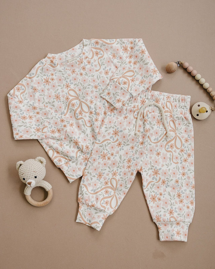 Baby wearing the Lucky Panda Kids Cozy Daisy cotton jogger set while lying on a cream quilt.
