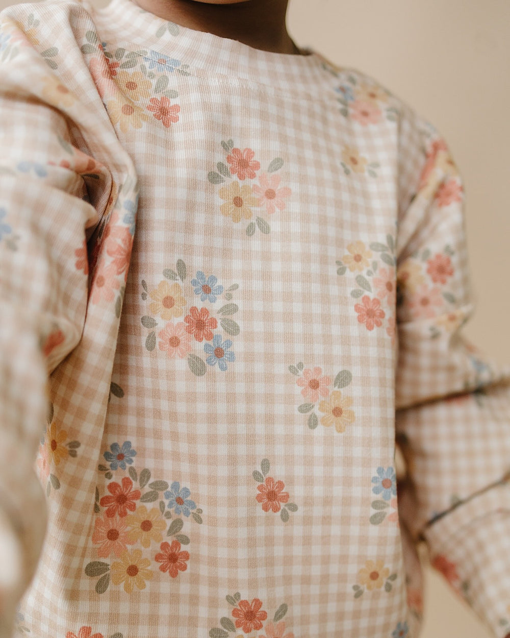 Baby wearing the Wild Flower cotton jogger set while lying on a cream quilt.