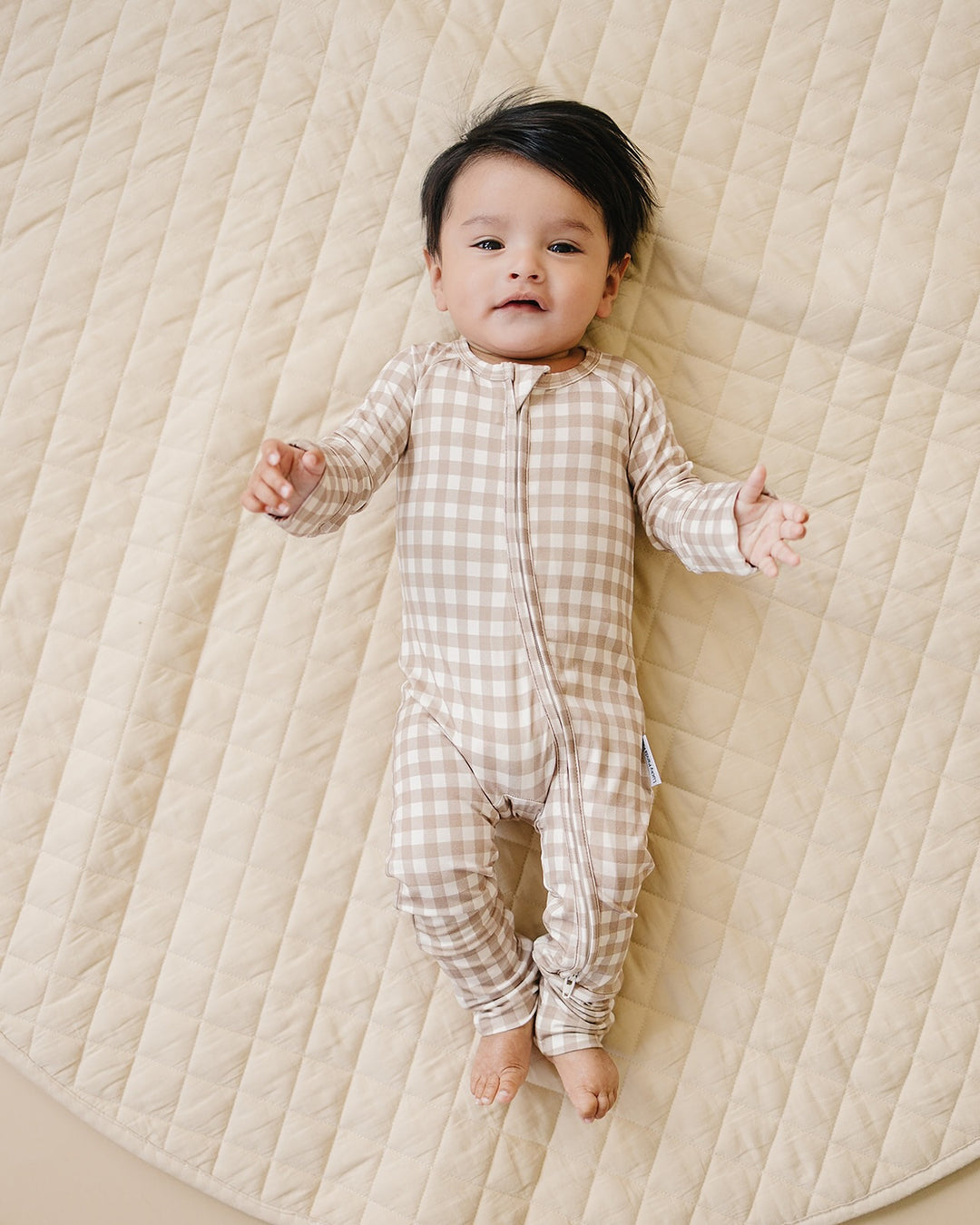 Baby lying comfortably in the Lucky Panda Kids Beige Gingham bamboo zip romper.