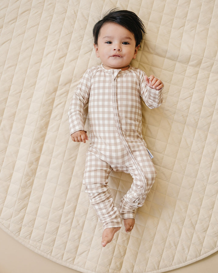 Full-length view of a baby wearing the Beige Gingham bamboo romper on a quilted blanket.