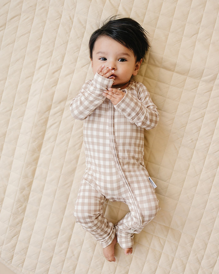 Baby wearing the Lucky Panda Kids Beige Gingham bamboo zip romper while lying on a cream quilt.