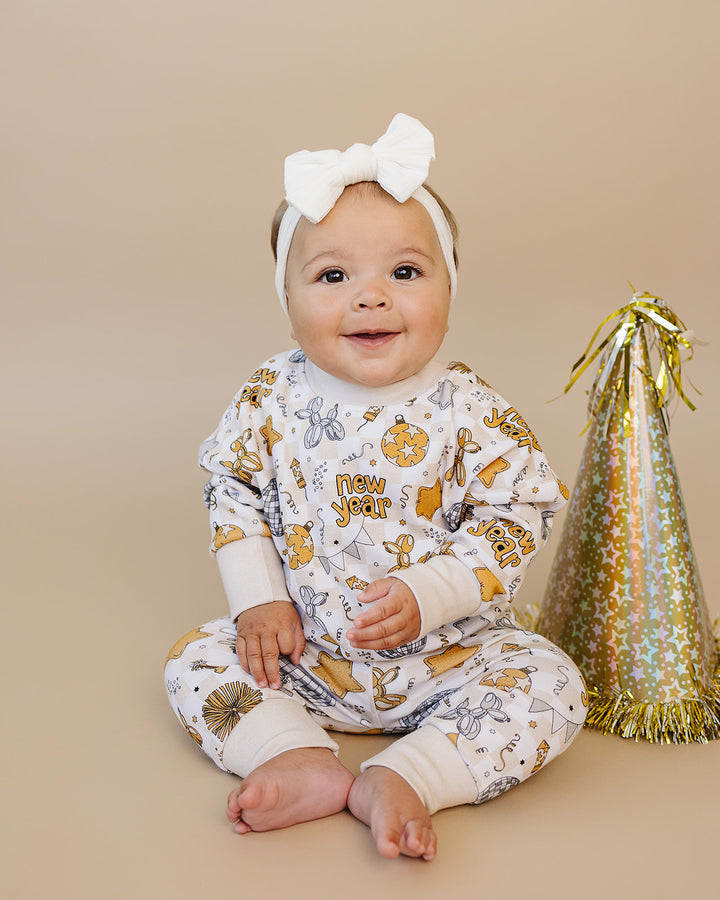 Baby wearing a New Year-themed outfit with a gold party hat on a beige background