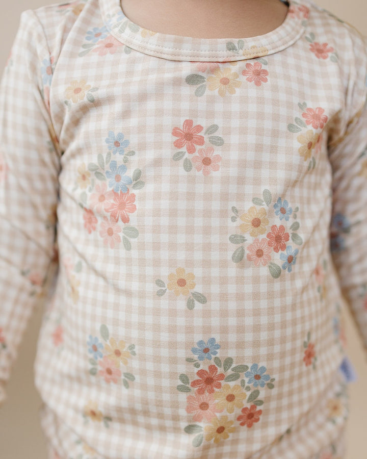 Toddler climbing onto a wooden chair in the Wild Flower bamboo zip romper, showing the back fit.