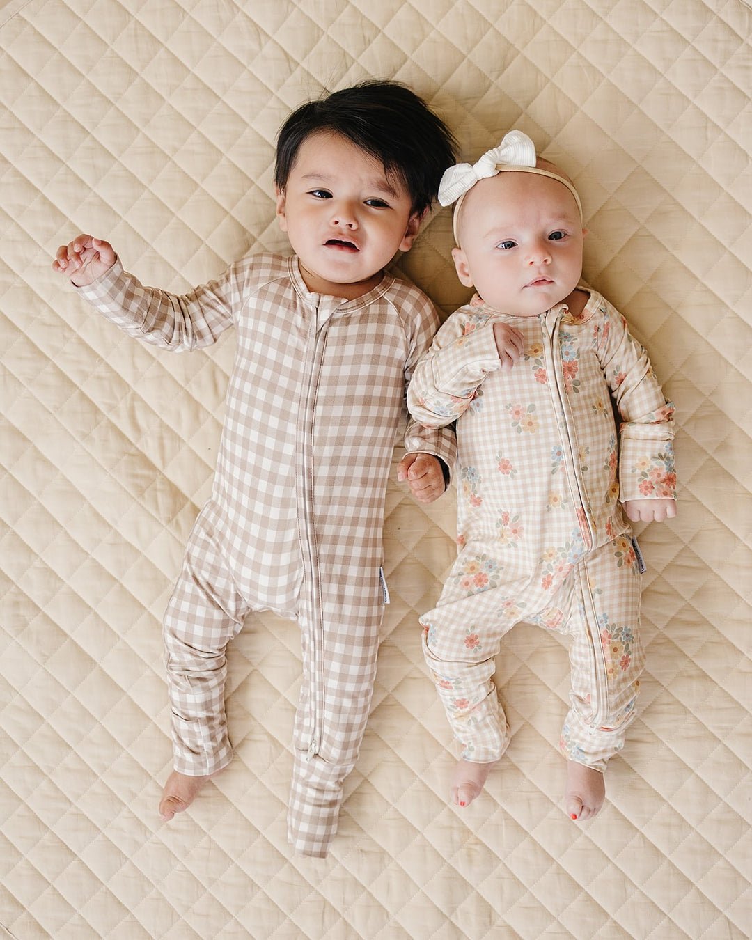 Two babies lying together in coordinating Lucky Panda Kids Beige Gingham and floral bamboo rompers.