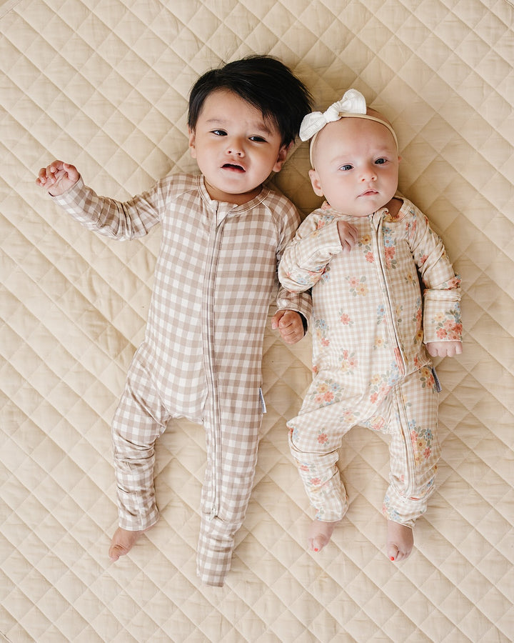 Two babies lying together in coordinating Lucky Panda Kids Beige Gingham and floral bamboo rompers.