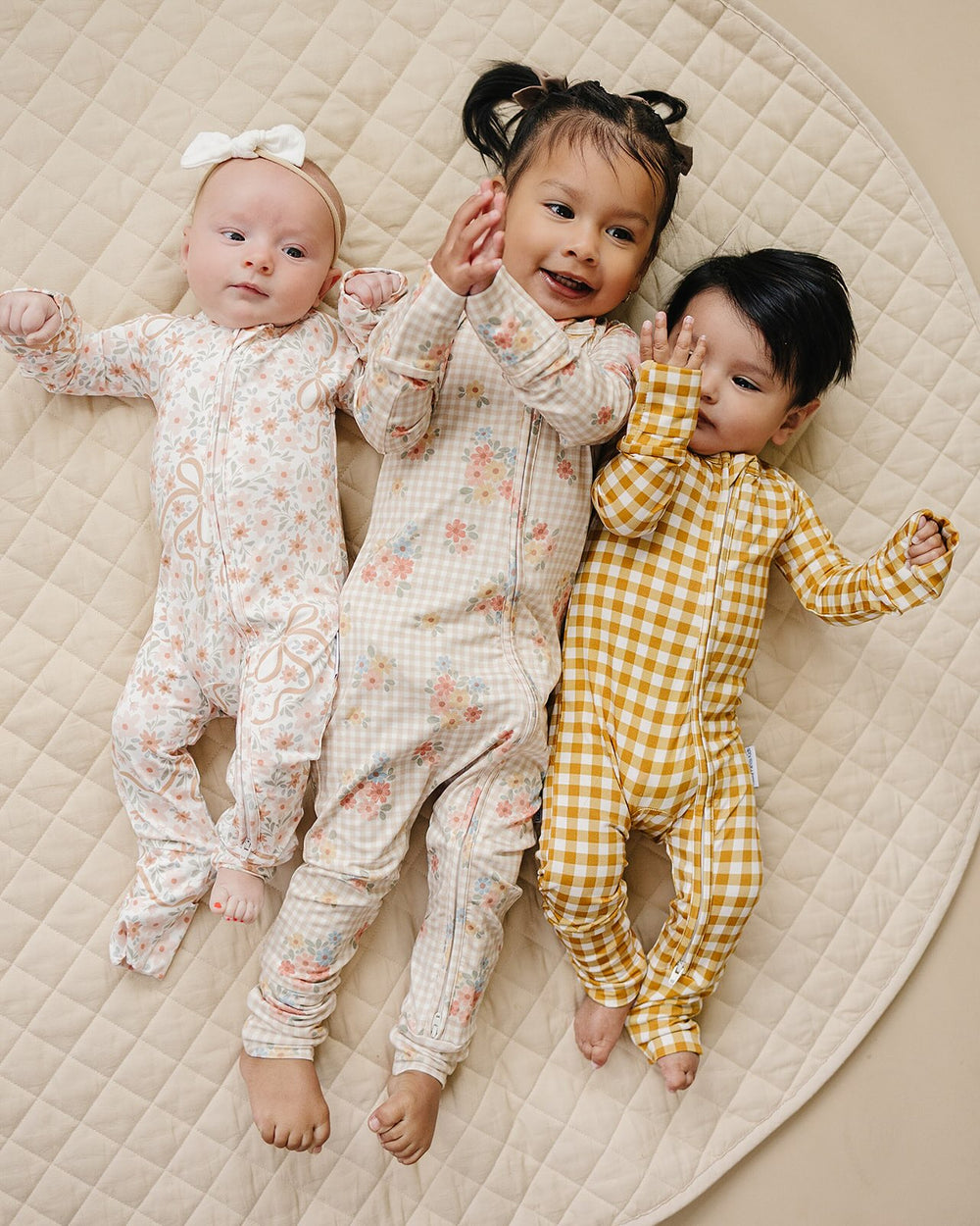 Three children wearing coordinating Lucky Panda Kids Yellow Gingham and floral bamboo zip rompers.