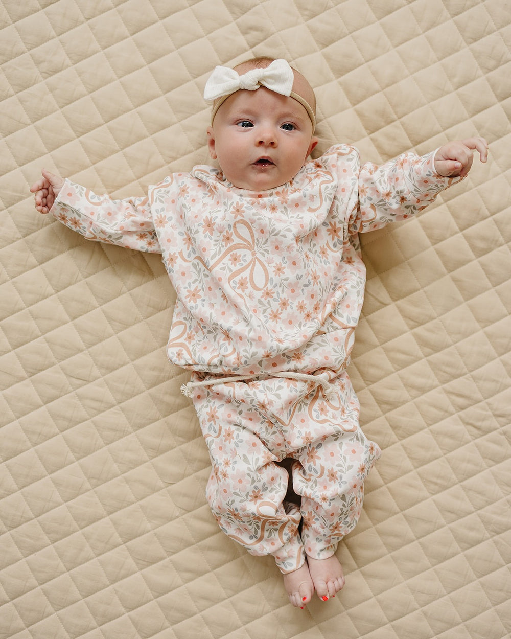 Baby wearing the Lucky Panda Kids Cozy Daisy cotton jogger set while lying on a cream quilt.
