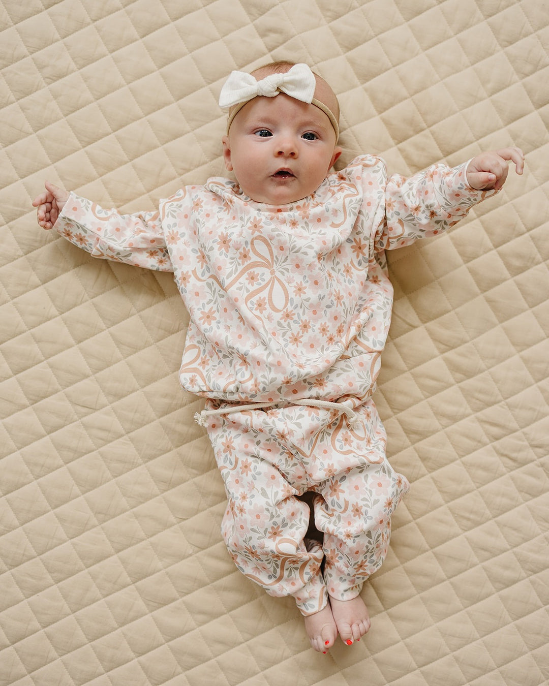 Baby wearing the Lucky Panda Kids Cozy Daisy cotton jogger set while lying on a cream quilt.

