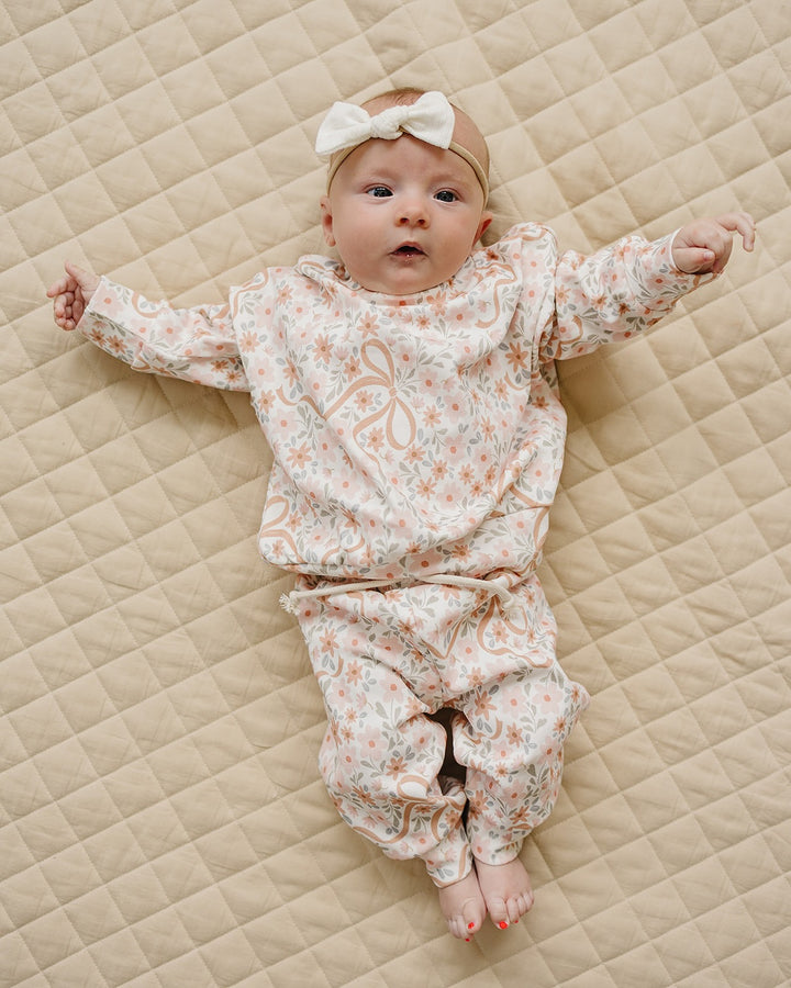 Baby wearing the Lucky Panda Kids Cozy Daisy cotton jogger set while lying on a cream quilt.

