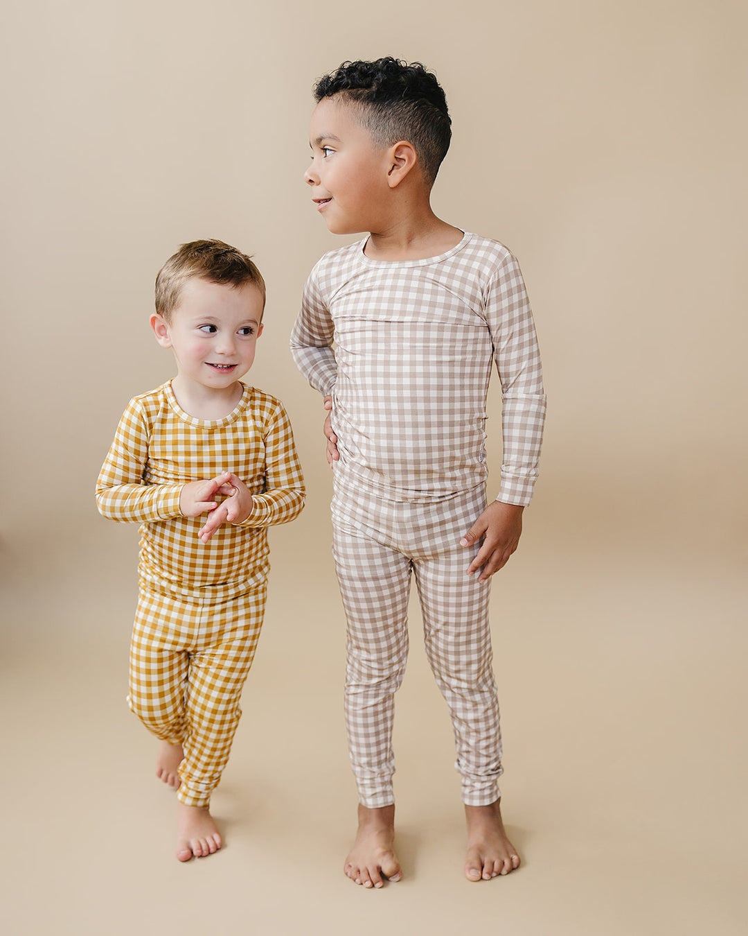 Two children standing together in matching Lucky Panda Kids Beige Gingham bamboo pajama sets.