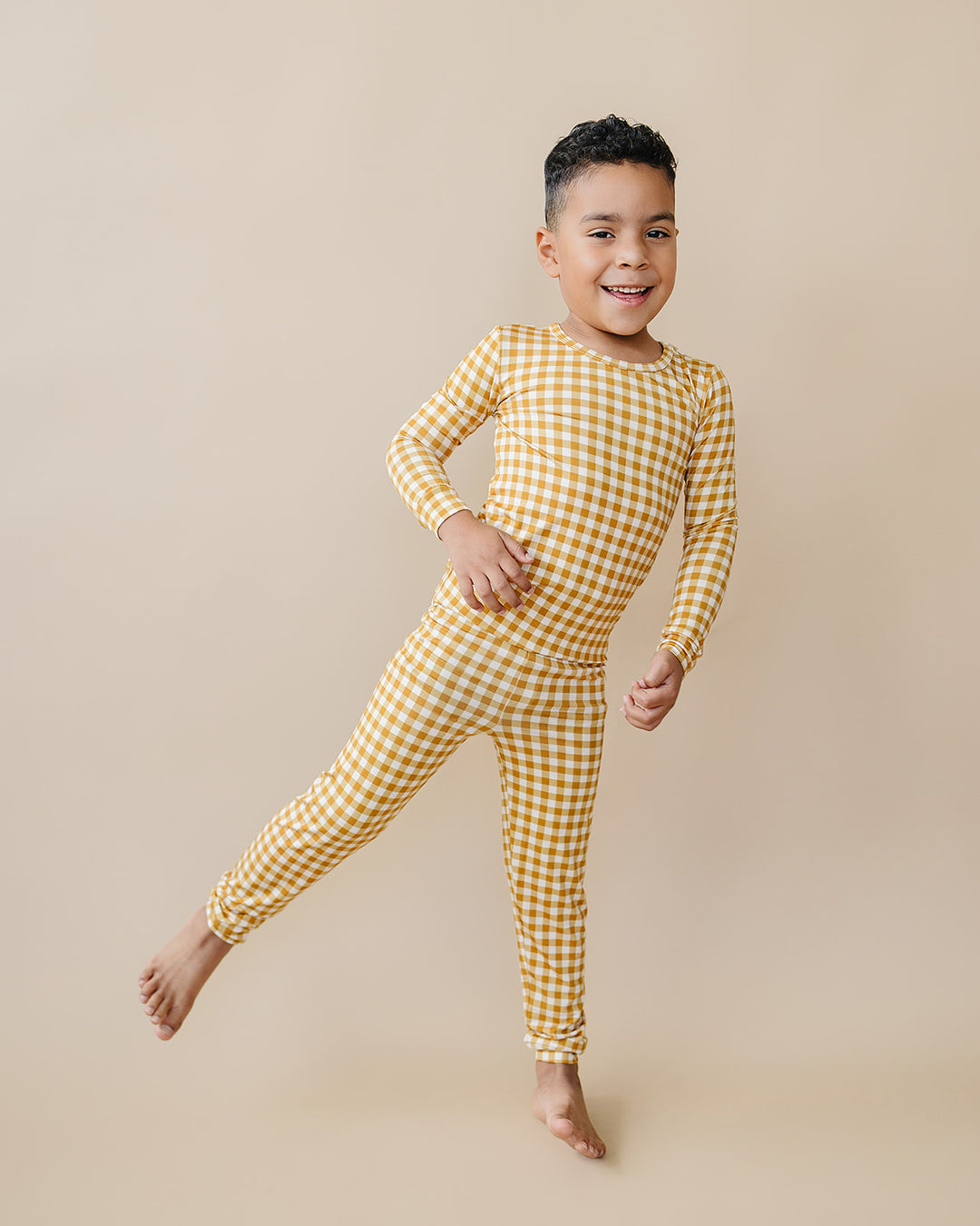 Child posing playfully in the Yellow Gingham bamboo pajama set, showing its flexible fit.