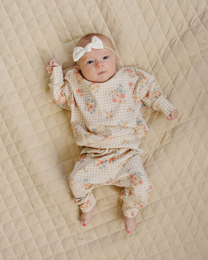 Baby lying on a cream quilt in the Lucky Panda Kids Wild Flower cotton jogger set.