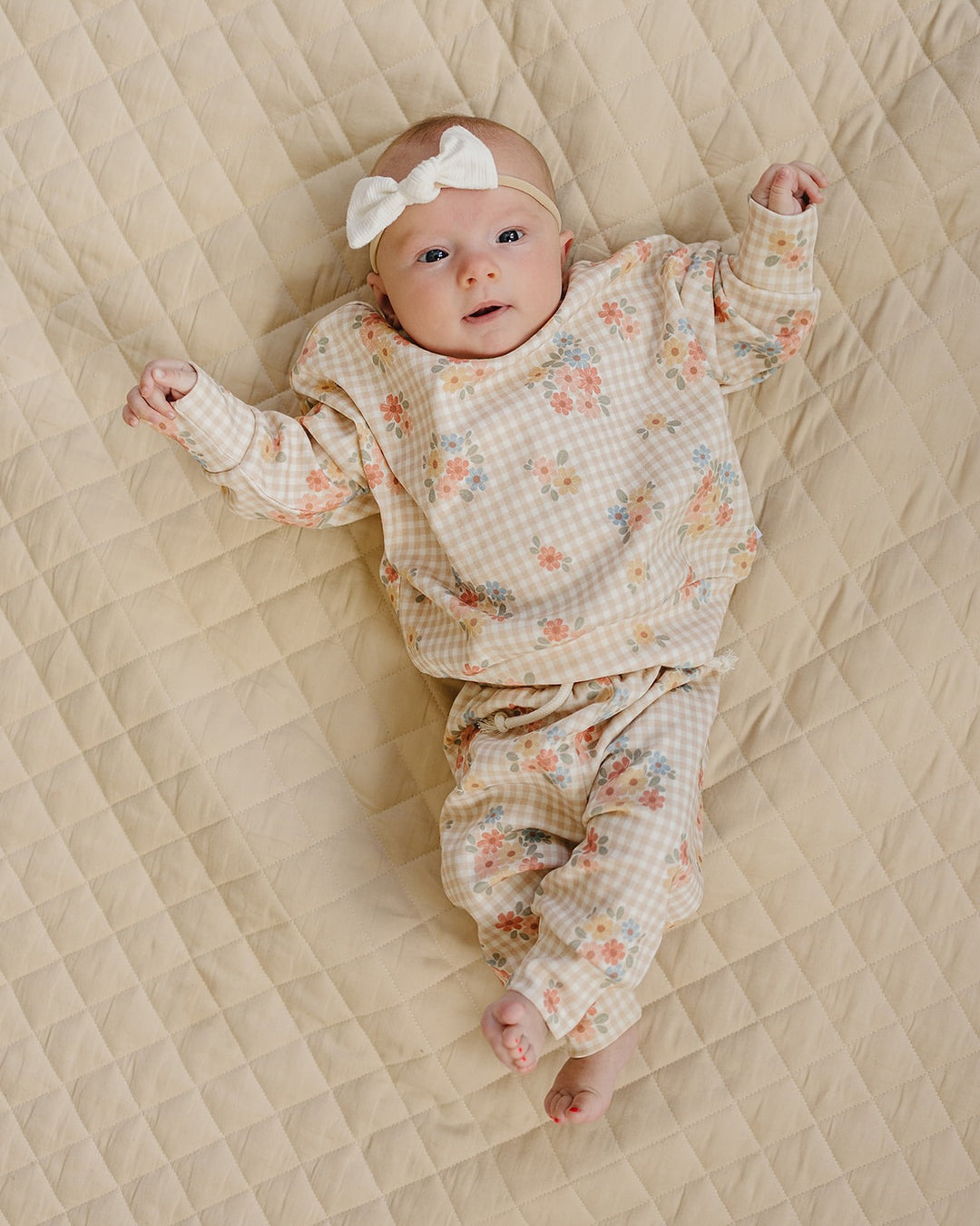 Baby wearing the Wild Flower cotton jogger set while lying on a cream quilt.