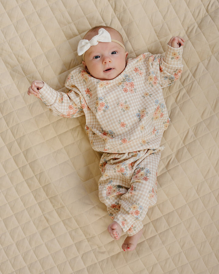 Baby wearing the Wild Flower cotton jogger set while lying on a cream quilt.