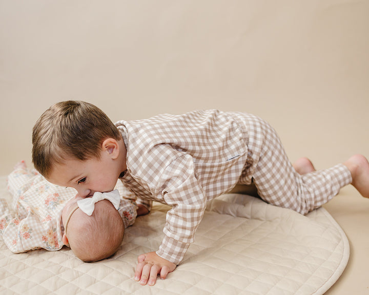 Child playing beside a baby wearing the Wild Flower cotton jogger set on a quilted blanket and boy wearing Beige Gingham Jogger Set.