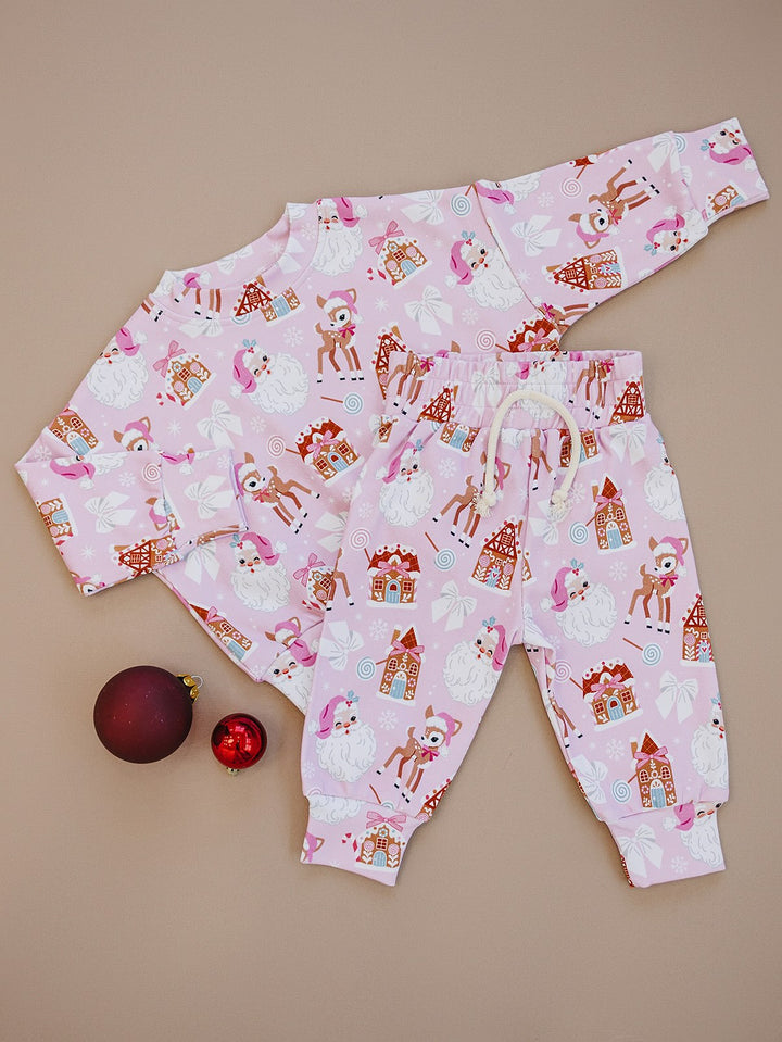 Pink Christmas long sleeve top and matching jogger pants laid flat beside holiday ornaments.