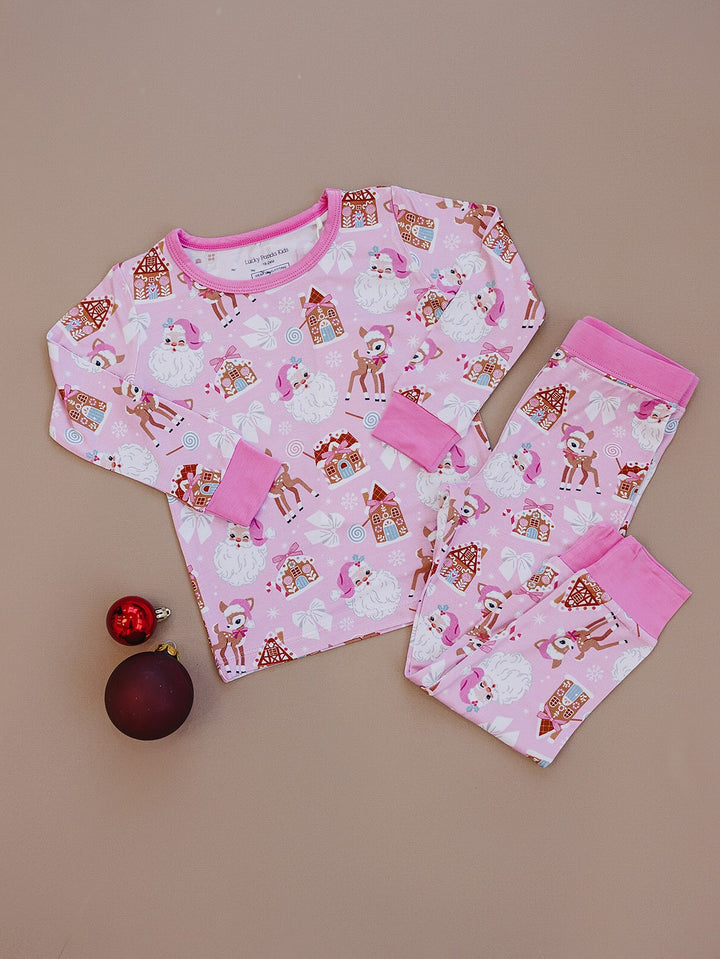 Pink Christmas two piece pajama set laid flat beside ornaments, showing the holiday print and pink trim.