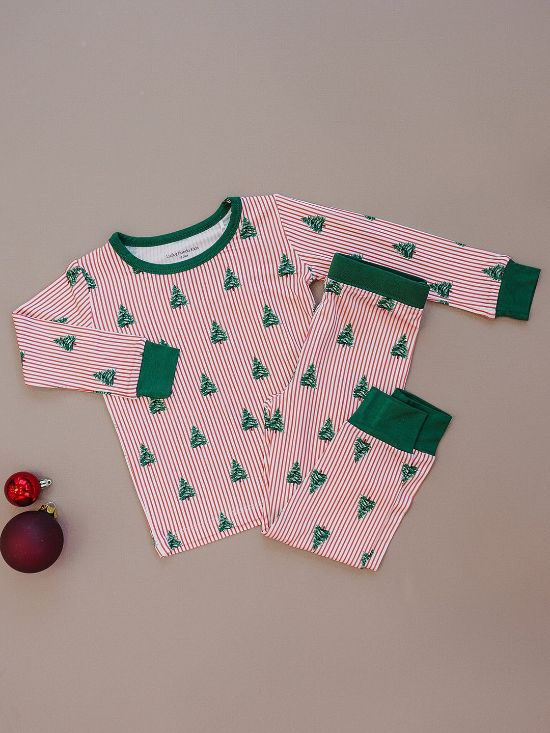 Magical Trees pajama top and matching pants laid flat beside Christmas ornaments.