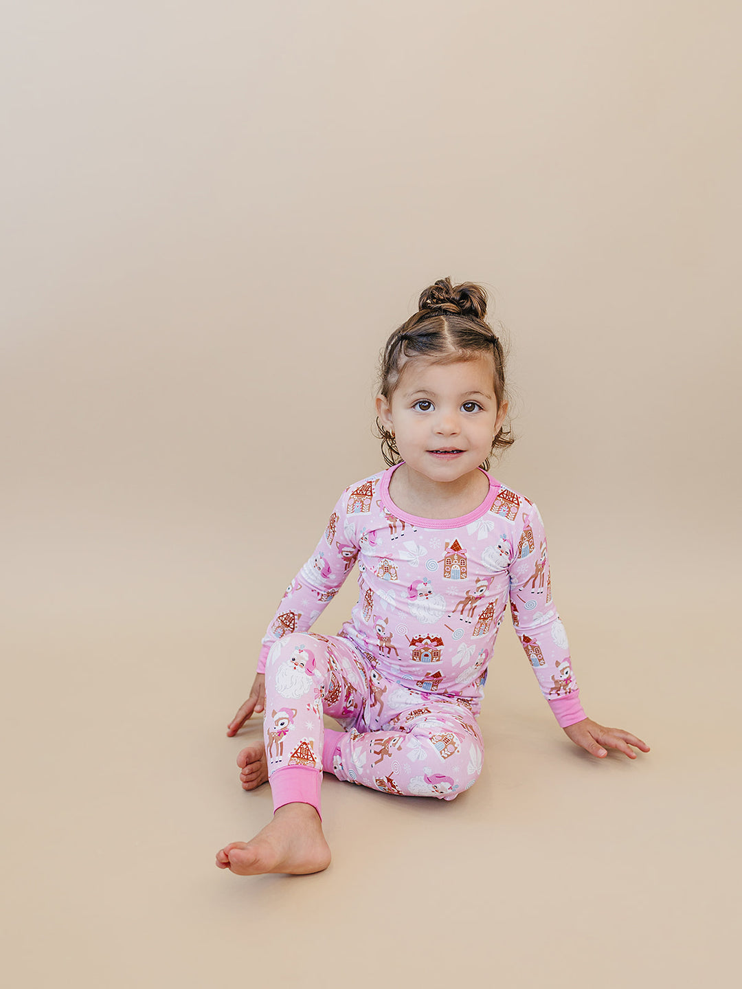 Toddler sitting on the floor in Pink Christmas pajamas with matching printed pants and pink cuffs.
